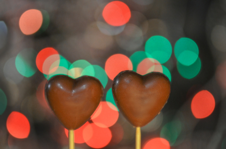 andy in the shape of a heart covered with chocolate on sticks. Love concept with chocolate heart shapes on bokeh defocused lights and shadowの写真素材