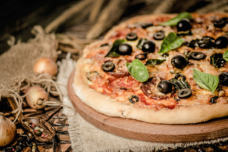 Traditional pizza with cheese, tomatoes, black olives, basil. Delicious italian pizza on wooden pizza board. Table top viewの写真素材