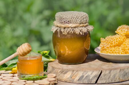Sweet honey in the comb.  Jars of honey, bee honeycomb  on wooden table with flowers backgroundの写真素材