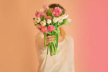 Young charming  smile girl holding big bouquet of tulips on light beige background. Young lovely girl in the white dress with colourful fresh flowers tulips
の写真素材