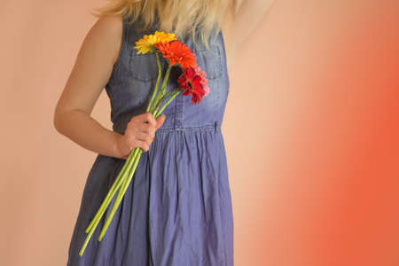 Cheerful young lady wearing denim dress and flowers chamomile in handsの写真素材