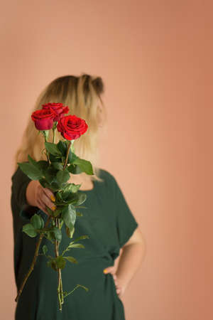 Portrait of young woman dressed in green dress holding bouquet of roses. Girl with bouquet of red rosesの写真素材
