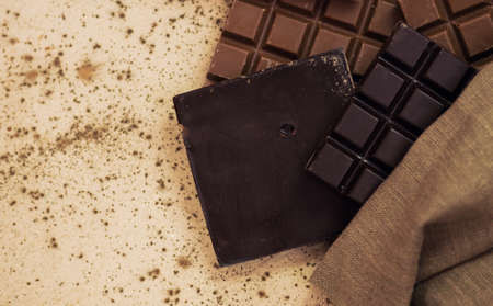 Different milk and dark chocolate. Chocolate pieces on wooden background. Dark, milk and white chocolate bar in burlap bagの写真素材