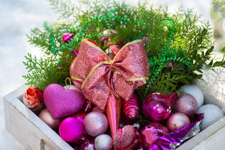Red New Year toys in a wooden box around Christmas tree. Christmas accessories and toys covered in snow in a wooden box outdoors.の写真素材