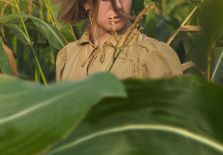 Woman with trendy gold makeup walking carefree in cornfield. Attractive young woman standing between green leaves in a corn field.の写真素材