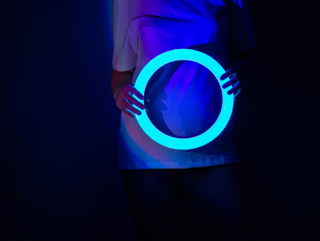 Cheerful young woman dance on the stage in abstract glowing colorful bright neon lighting. Charming young model in vibrant neon fantastic glowing dance during performs on stage.の写真素材
