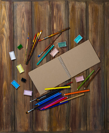 Work space artist or designer mock up with craft tools on a wooden background. Mock up notebook album and objects for painting top view on a wooden background.の写真素材
