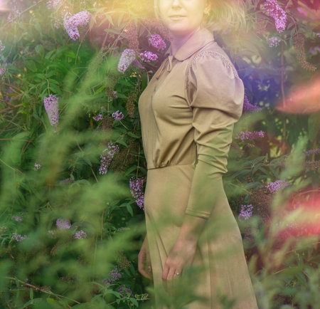 Happy woman in buddleia flowers field in luxurious gold dress.Young woman in gold dress standing in flowers field.の写真素材