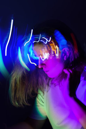 Cheerful young woman elegantly dressed dancing in futuristic colorful bright modern neoned colors glowing light.の写真素材