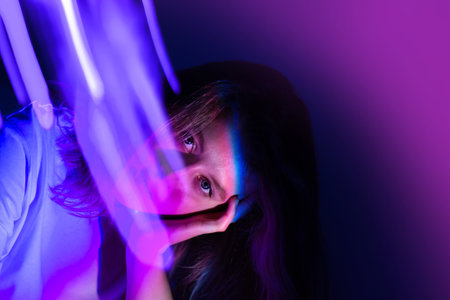Cheerful young woman in neon electric glow backdrop. Pretty happy woman with bright fluorescent illumination photographic effect.の写真素材