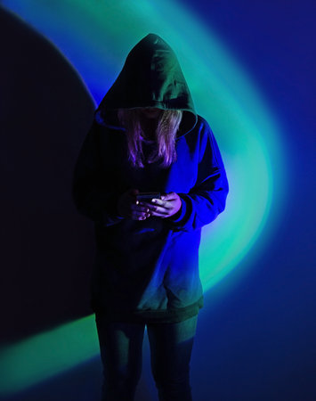 Safe storage of personal data on a smartphone. Shrouded in darkness hooded figure with phone on vivid neon background.の写真素材