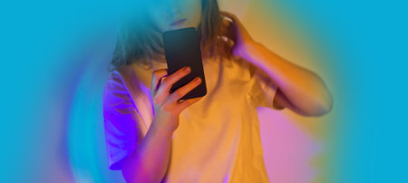 Woman holding a smartphone and chatting online by neon shining lights. communication in a pleasant conversation.の写真素材