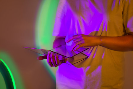 Attractive woman in white shirt with digital tablet surrounded by colorful bright work ambiance. Engaging contemporary technology and beautiful girl in white shirt using digital tablet in colorful multicolored light.の写真素材