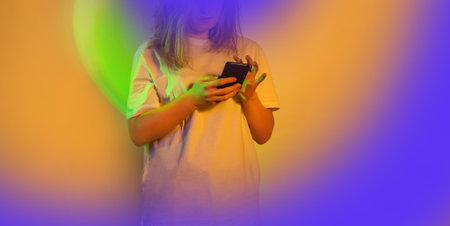 Cheerful young woman writes a text message with her mobile. Woman using mobile phone to give feedback on a neon glowing backgroundの写真素材
