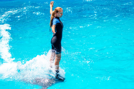 A young girl trains Glad beautiful dolphin in blue water in the pool on a bright sunny day on the original submission for touristsのeditorial素材