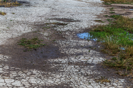 Damaged road, cracked asphalt sword with potholes and spots, Ukraine. Very bad asphalt road with large holes. Terrible technology construction roads. Numerous dangerous failures. Bad road. Road repairの写真素材