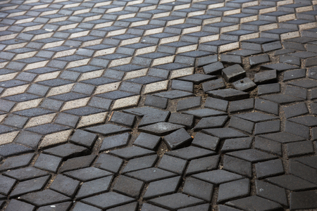 Damaged asphalt road with potholes, caused by freeze-thaw cycles in winter. Bad road. Broken pavements sidewalks on sidewalk. pavement with paving slabs with defects and cracks coming in perspectiveの写真素材