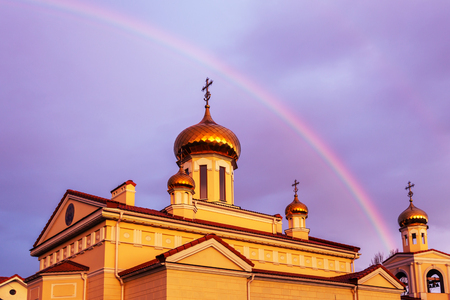 The golden domes of the Orthodox Christian church in the rays of the evening sun setting against the background of a bright multi-colored rainbow after the rain. Rainbow, Good News, Gospelの写真素材
