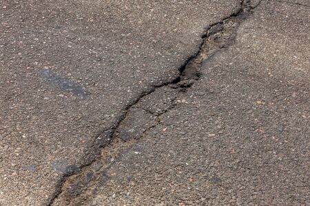 Damaged road, asphalt cracks. Asphalt with potholes and asphalt overflow spots. Very bad asphalt road with big holes. Scary technology in road construction. Numerous dangerous failures.の写真素材