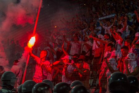 ODESSA, UKRAINE -July28,2019: Fanatical fans in stand during game of eternal rivals. Fans on racks are happy, glow with fire and waving flag. Fiery show at stadium. Fan of hooligan light fiery flasheのeditorial素材