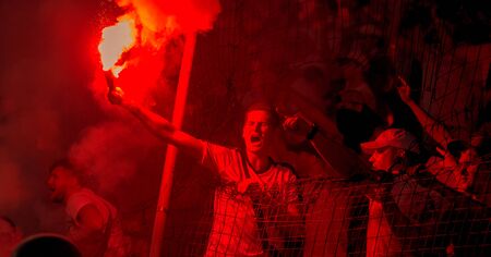 ODESSA, UKRAINE -July28,2019: Fanatical fans in stand during game of eternal rivals. Fans on racks are happy, glow with fire and waving flag. Fiery show at stadium. Fan of hooligan light fiery flasheのeditorial素材