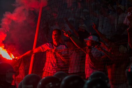 ODESSA, UKRAINE -July28,2019: Fanatical fans in stand during game of eternal rivals. Fans on racks are happy, glow with fire and waving flag. Fiery show at stadium. Fan of hooligan light fiery flasheのeditorial素材