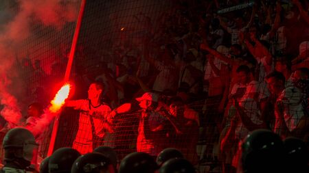 ODESSA, UKRAINE -July28,2019: Fanatical fans in stand during game of eternal rivals. Fans on racks are happy, glow with fire and waving flag. Fiery show at stadium. Fan of hooligan light fiery flasheのeditorial素材