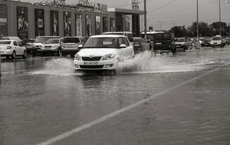 Odessa, Ukraine - August 9, 2019: driving car on flooded road during flood caused by torrential rains. Cars float on water, flooding streets. Splash on the car. Flooded city road with a large puddleのeditorial素材
