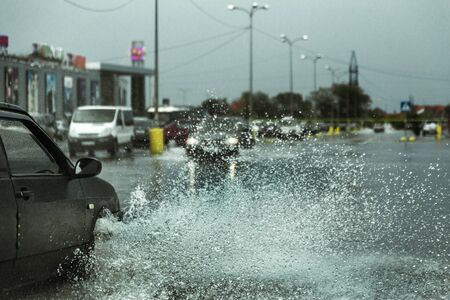 Driving car on flooded road during flood caused by torrential rains. Cars float on water, flooding streets. Splash on the car. Flooded city road with a large puddleのeditorial素材