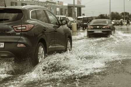 Odessa, Ukraine - August 9, 2019: driving car on flooded road during flood caused by torrential rains. Cars float on water, flooding streets. Splash on the car. Flooded city road with a large puddleのeditorial素材