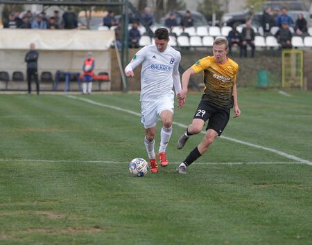 ODESSA, UKRAINE-CIRCA 2019: Footballers of local football team during game in regional Derby championship on a bad football pitch. Hot moment of football match on grass green field of the stadiumのeditorial素材