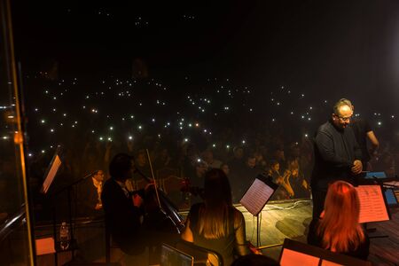 Odessa, Ukraine-circa 2019: Dark background Bright lights music show.  Rock concert and Symphony orchestra.  Conductor, musical instrument on concert stage of theater. Orchestral instruments on stageのeditorial素材