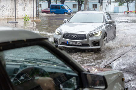 Odessa, Ukraine - May 28, 2020: driving car on flooded road during flood caused by torrential rains. Cars float on water, flooding streets. Splash on car. Flooded city road with large puddleのeditorial素材