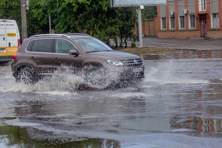 Odessa, Ukraine - May 28, 2020: driving car on flooded road during flood caused by torrential rains. Cars float on water, flooding streets. Splash on car. Flooded city road with large puddleのeditorial素材