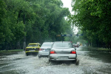 Odessa, Ukraine - May 28, 2020: driving car on flooded road during flood caused by torrential rains. Cars float on water, flooding streets. Splash on car. Flooded city road with large puddleのeditorial素材