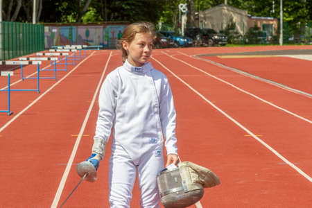 Odessa, Ukraine - June 9, 2020: Young female athlete wearing a mask and white fencing costume on the...
