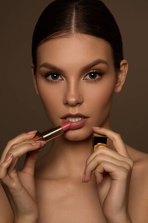 Beautiful girl with perfect skin on a brown background paints lips with lipstick.の写真素材