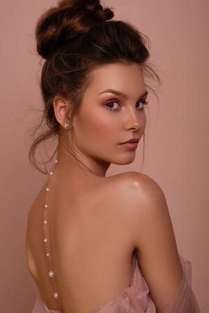 Beautiful young woman with perfect skin, beautiful hairstyle and open back on a pink background.の写真素材