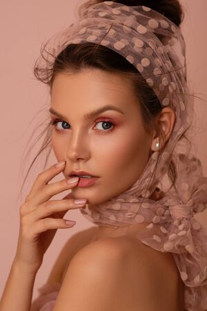Beautiful young woman with perfect skin in a scarf on a pink background.の写真素材