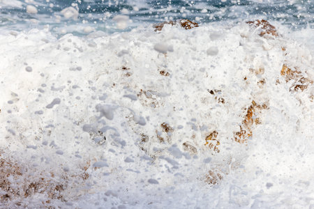 waves hitting a red orange rock in Spain.の写真素材