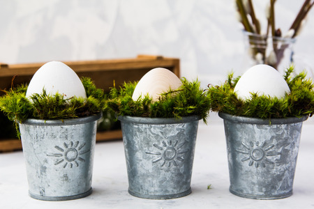 Three eggs stand in iron cups with moss