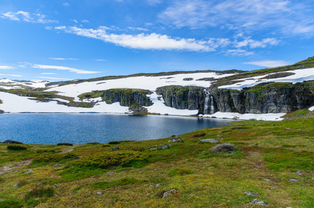 Highland norwegian summer landscape with lake waterfall and snowの写真素材