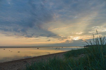 Calm and colourful cloudscape sunrise at sea gulf with tall grass on beachの写真素材