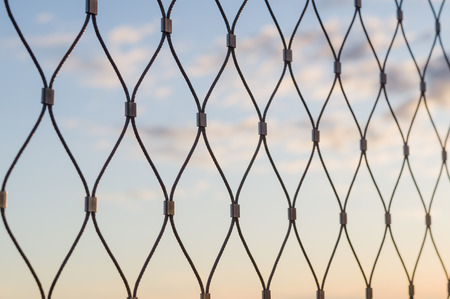 Metal mesh wire fence closeup sunset sky backgroundの写真素材