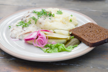 Mashed potatoes with creamy mushroom sauce, pickled cucumber, red onion and slice of bread. Image...