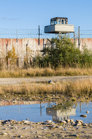Abandoned watch-tower and prison wall with reflection in puddleの写真素材