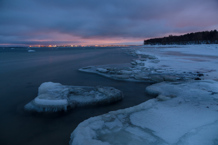 Winter landscape of frosty seacoast and city lights by night, long exposureの写真素材