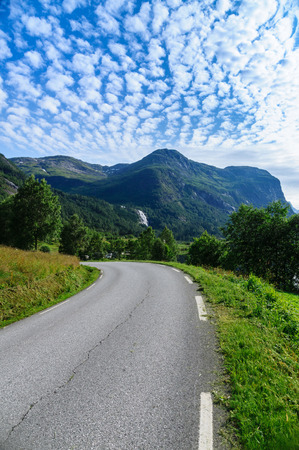 Narrow curvy road with scenic background of mountains and clouds, Norwayの写真素材
