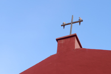 Two pigeons on the wooden cross of red church against blue skyの写真素材