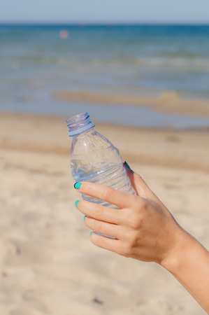 Female hand holding opened bottle of water against beach backgroundの写真素材